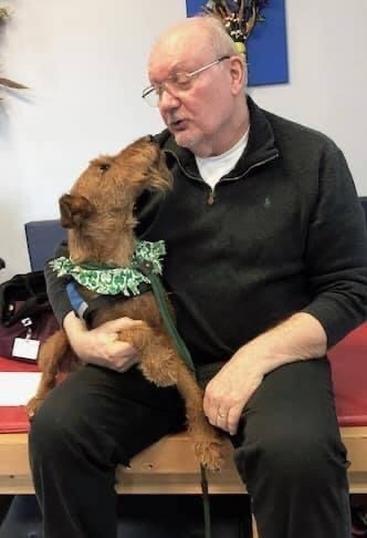 A guardian seated indoors beside his credentialed therapy dog.